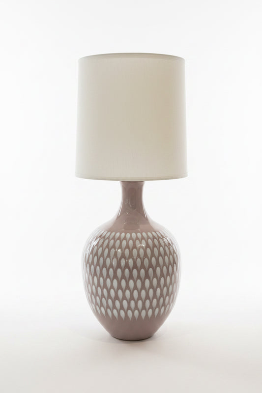Dusty lavender 70’s style lamp by The Vault Creative with a vintage design and ceramic base, shown turned on with warm light.