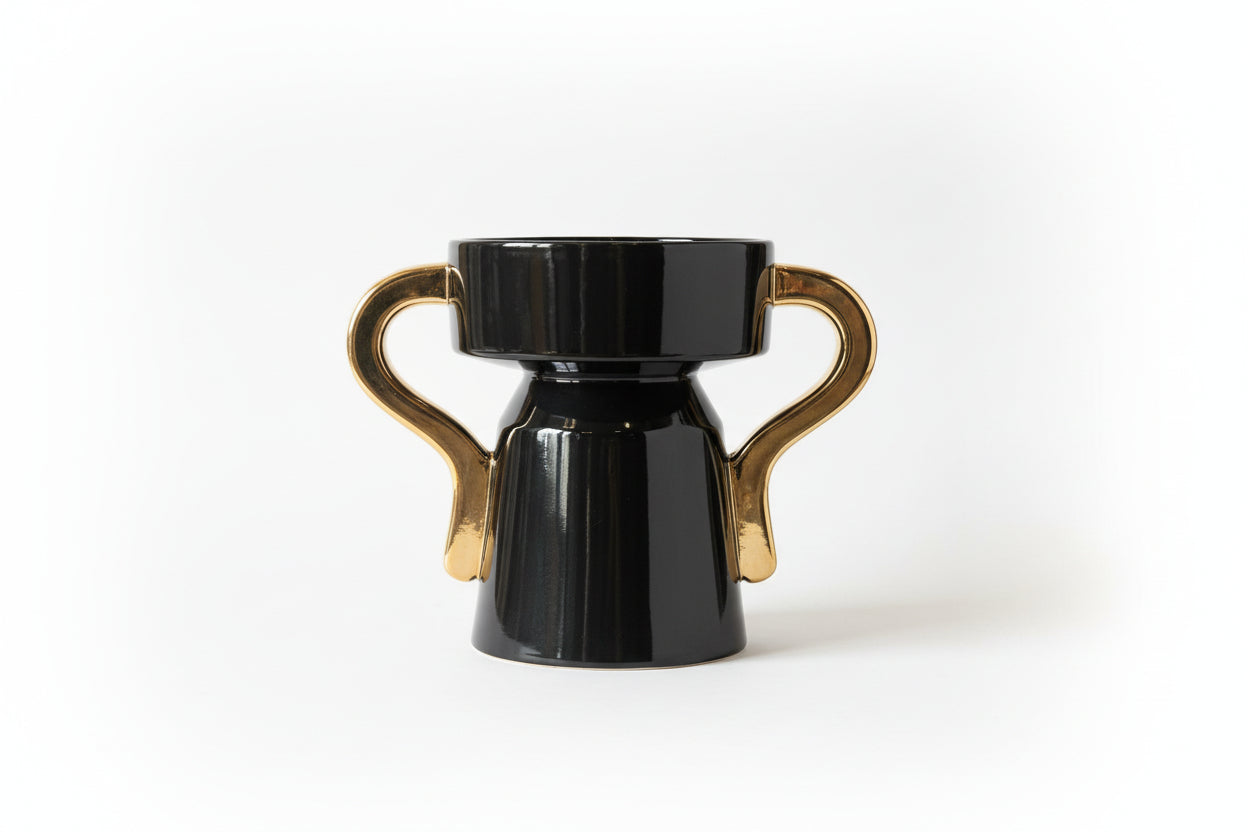 A black and gold ceramic vase with gold handles, displayed against a patterned backdrop.