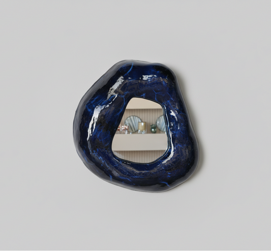 A small ceramic mirror with a blue and black patterned frame, mounted on a wall.